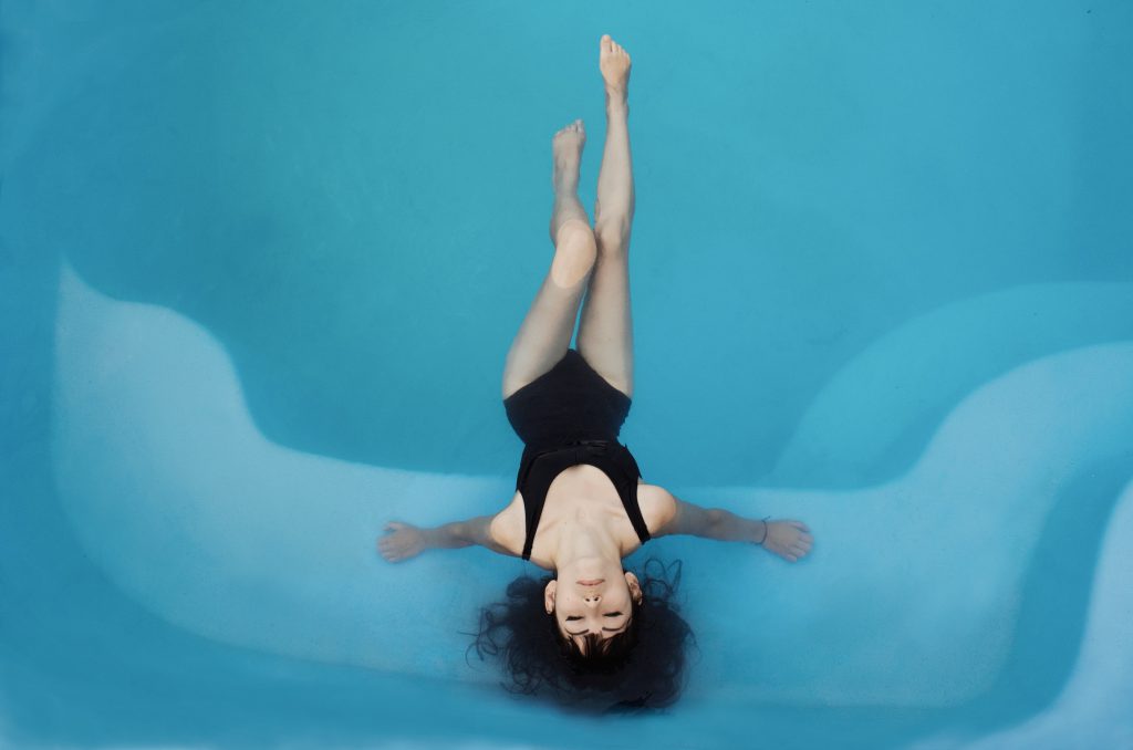 woman floating in a swimming pool wearing a one-piece swimsuit